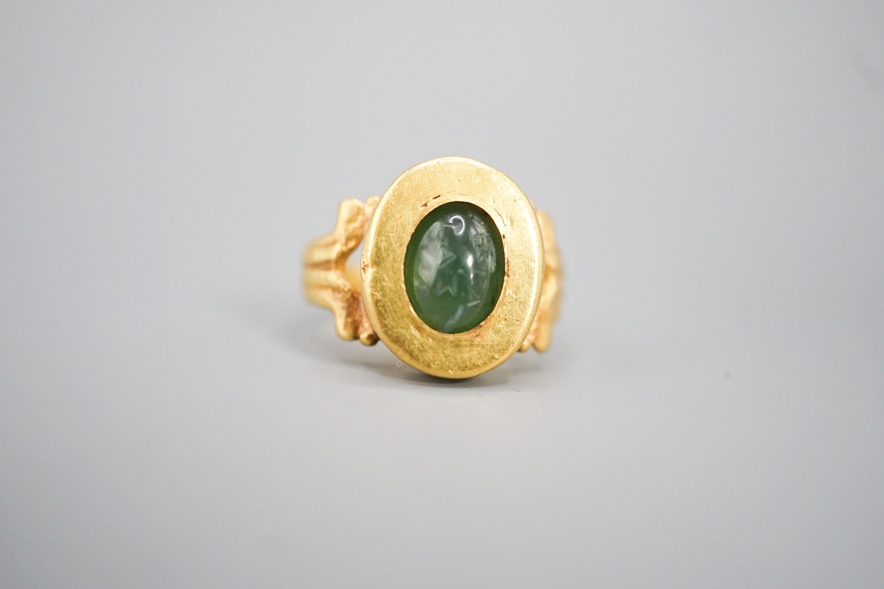 An antique yellow metal and carved nephrite? oval ring, size H, gross 4 grams (the stone is loose in situ and needs re-setting).